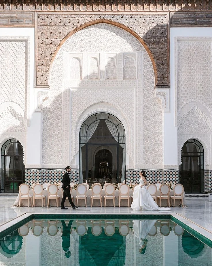 Les mariés au bord d’un bassin devant une façade à l’architecture marocaine