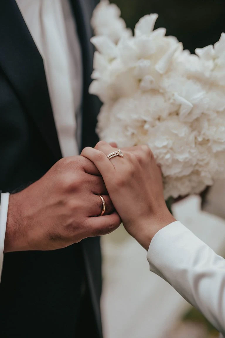Les mains des mariés et un bouquet de fleurs blanches